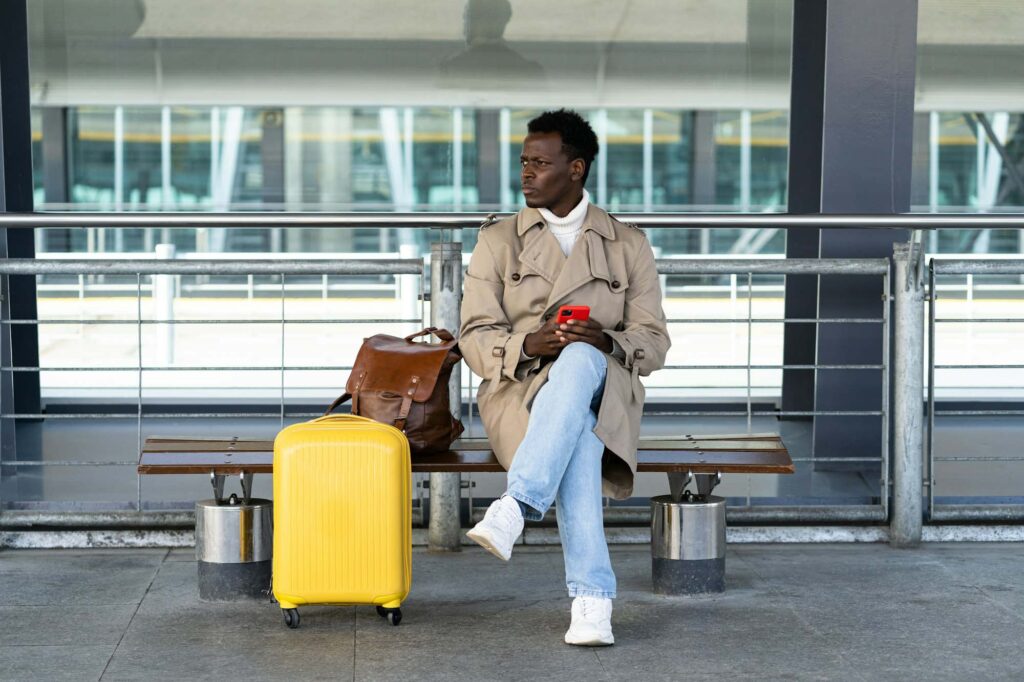 black-traveler-man-with-suitcase-sitting-on-bench-in-airport-terminal-calling-and-looking-for-taxi.jpg